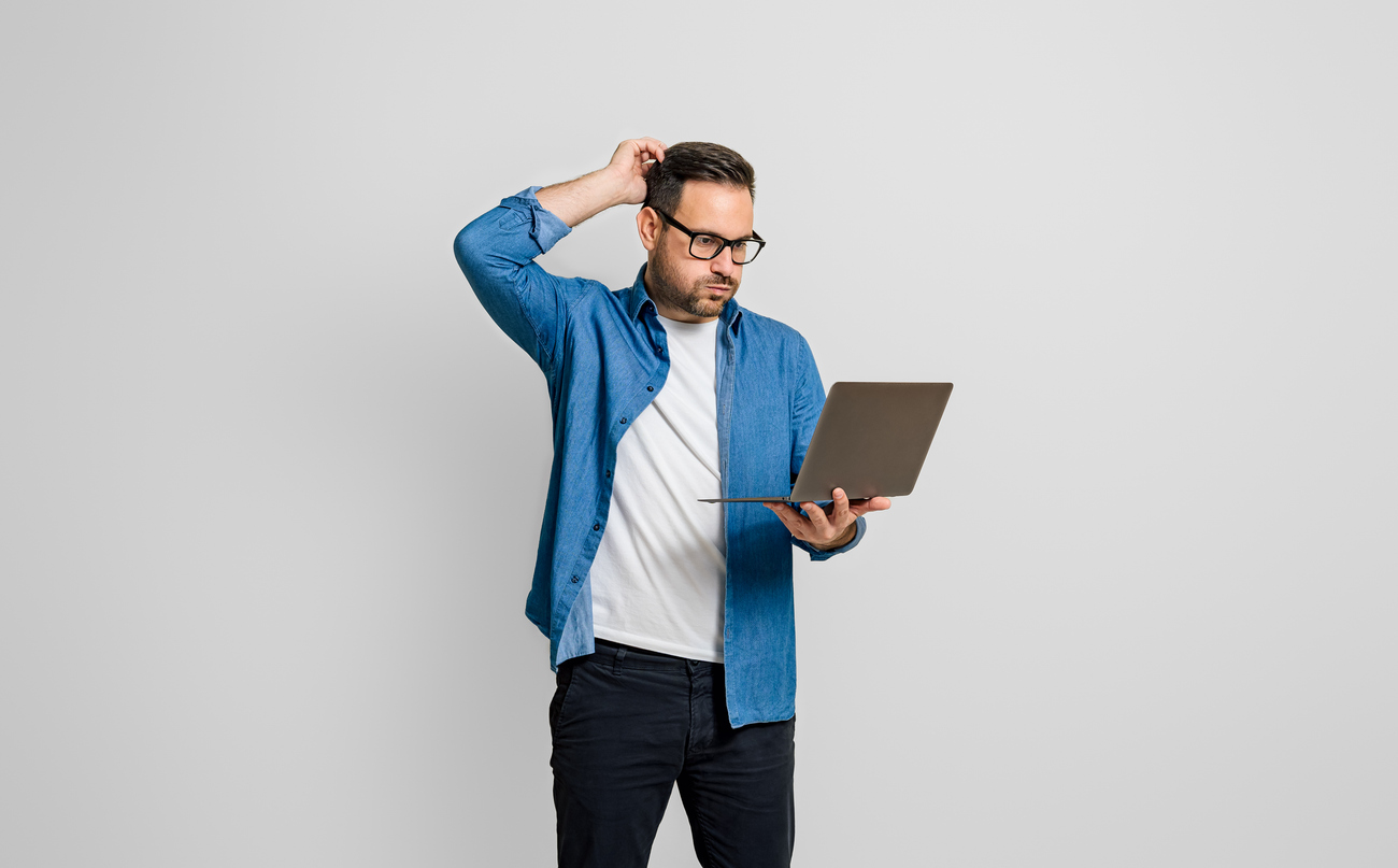 man struggling with his laptop, scratching his head and holding a laptop